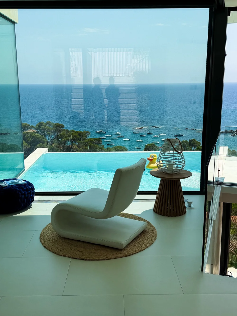 A chair by the glass wall, facing the infinity pool